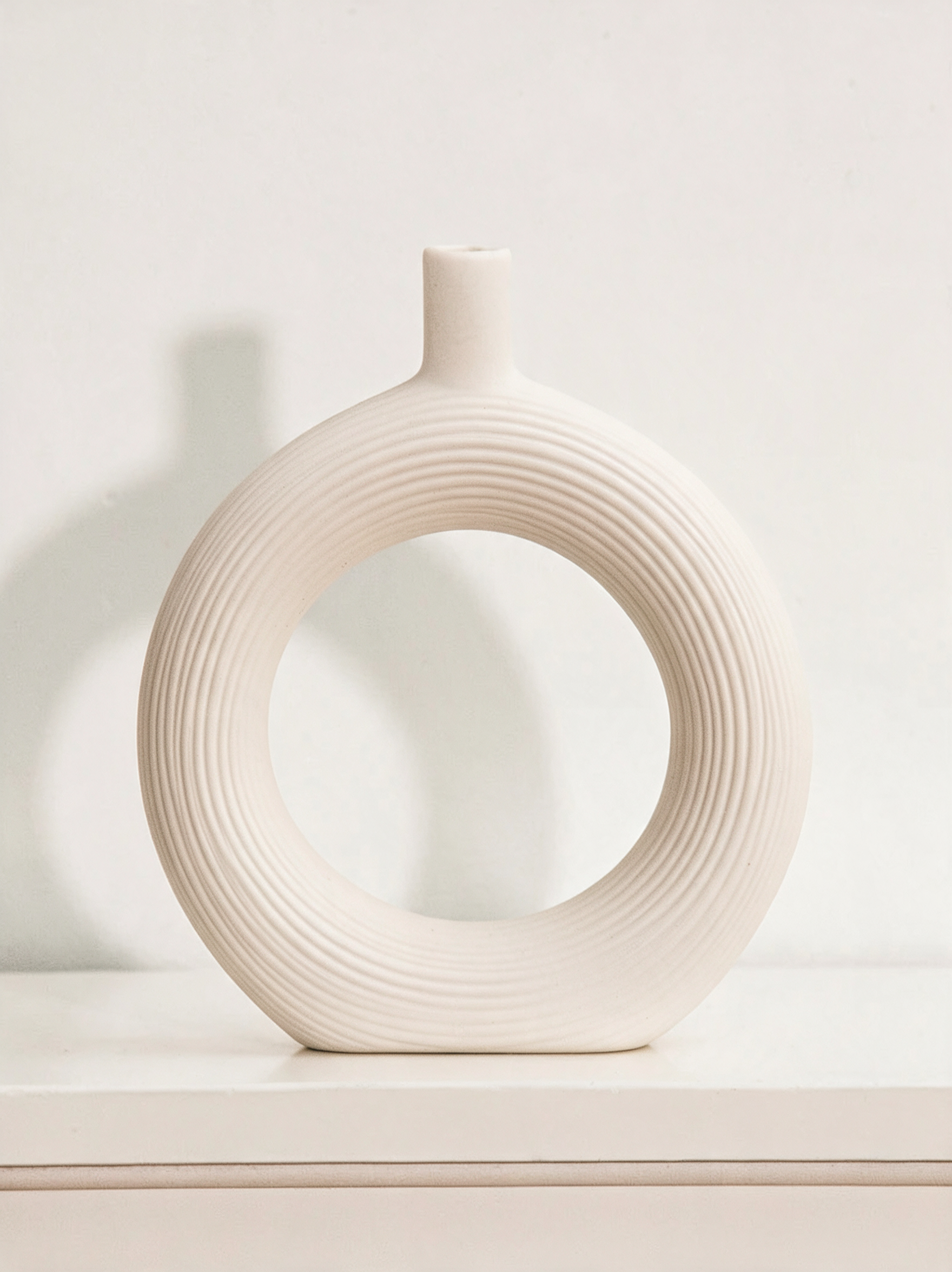 Vase Arche anneau en céramique blanc cassé posé sur une console, lumière rasante